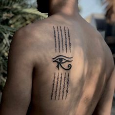 the back of a man with an eye tattoo on his left shoulder and words written in black ink