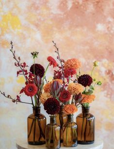 three glass vases with flowers in them on a marble table next to a wall