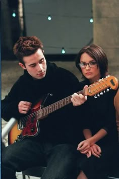 a man and woman sitting next to each other while playing the guitar in front of them