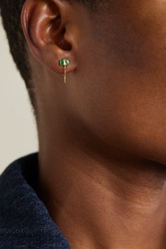 a close up view of a person wearing earrings with green stones on the end of their ear