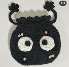 a crocheted black purse with white eyes and stars on the front, has two small flowers at the top