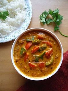 a bowl of curry next to a plate of rice and cilantro on a table