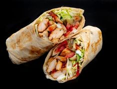 two burritos with meat, lettuce and tomato on black paper wrapper