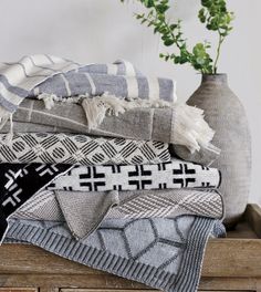 a stack of blankets sitting on top of a wooden table next to a vase filled with flowers