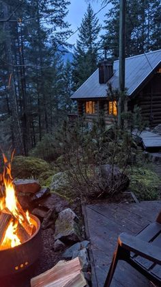 a fire pit sitting in the middle of a forest next to a wooden table and chairs