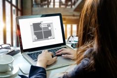 a woman sitting at a table with a laptop computer in front of her, on which she is working