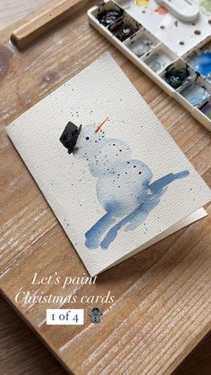 a snowman is on the table next to some paintbrushes and watercolors