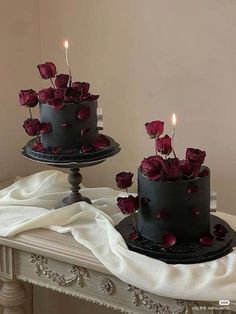 two black cakes with red roses on top and candles in the middle are sitting on a table