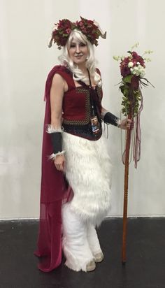 a woman dressed in costume standing next to a pole with flowers on top of it