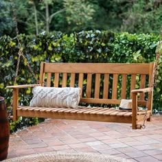 a wooden swing with pillows on it in the middle of a brick patio surrounded by greenery