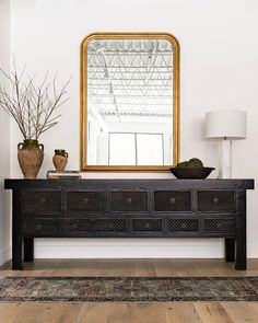 a large mirror sitting on top of a wooden table next to a lamp and vases