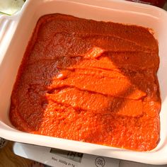 a white dish filled with red sauce on top of a wooden table