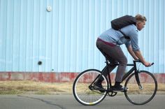 a man riding a bike down a street past a blue building with a red stripe on it