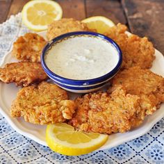 fried chicken on a plate with ranch dressing and lemon wedges next to the bowl