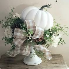 a white pumpkin decorated with flowers and greenery sits on a wooden table in front of a wall