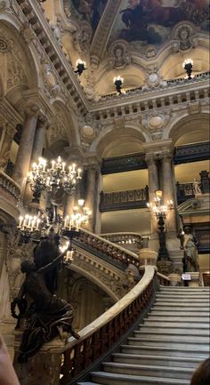 an ornate staircase with chandeliers and paintings on the walls in a large building