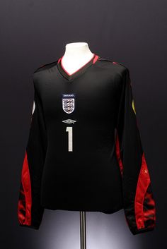 a black jersey with red and white stripes on it, sitting on a stand in front of a dark background