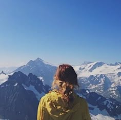 a woman standing on top of a snow covered mountain looking down at the valley below