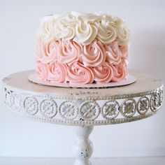 a pink and white frosted cake sitting on top of a metal stand next to a wall