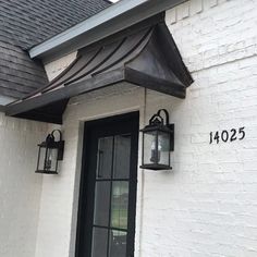 a white brick house with two black lanterns on the front door and numbers painted on the side