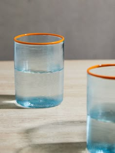 two glasses sitting on top of a wooden table next to each other and one has an orange rim