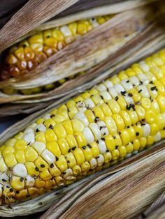 two corn cobs with black seeds and yellow kernels on the top one is half eaten