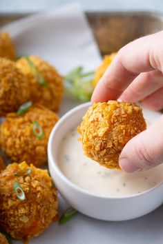 a person dipping something into a small white bowl filled with ranch dip and fried meatballs