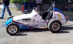 a white and blue race car sitting on top of a brick road next to people