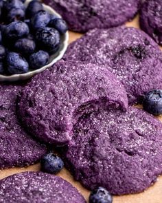 blueberry cookies with powdered sugar are on a cutting board next to a bowl of blueberries