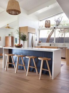 a kitchen with three stools next to an island in front of a window and potted plant on the counter