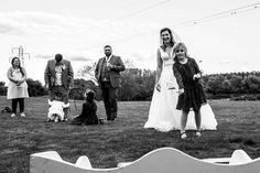 a bride and groom walking their dogs in the grass with other people standing behind them