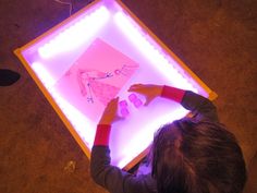 a young boy is drawing on a lit up light box with his hands and fingers