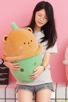 a woman holding a large stuffed animal in front of a pink wall with other toys