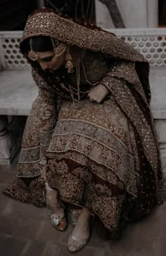 a woman sitting on top of a wooden bench wearing a brown and gold dress with an elaborate shawl