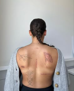 the back of a woman with tattoos on her upper and lower back, sitting in front of a white wall