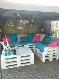 a couch made out of wooden pallets under a tent with blue and pink pillows