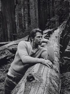 a man leaning on a fallen tree in the woods with his hand on his chin