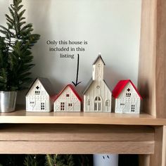 a shelf with three small houses on top of it and a potted tree in the background