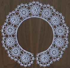 a white doily on a wooden surface with an oval design in the center and small flowers at the bottom