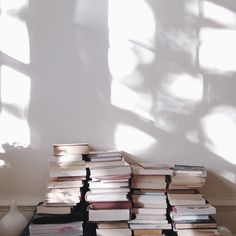 a stack of books sitting on top of a wooden table next to a vase and window