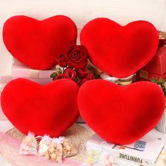 three red heart shaped cushions sitting on top of a pile of books next to roses