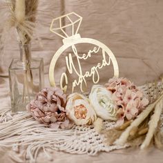 there is a wedding cake topper on the table with flowers and feathers next to it