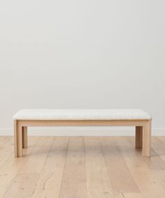 a wooden bench sitting on top of a hard wood floor next to a white wall