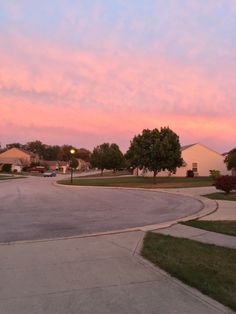 an empty street at dusk with pink clouds in the sky and green grass on either side