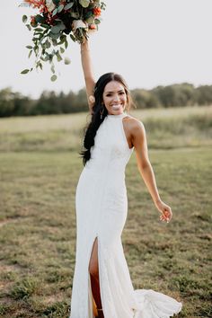 a woman in a long white dress holding a bouquet on top of her head and smiling at the camera