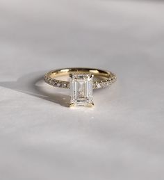 a gold ring with an emerald cut diamond in the center and pave set diamonds around the band