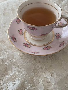 a tea cup and saucer sitting on a lace tablecloth with pink flowers in it