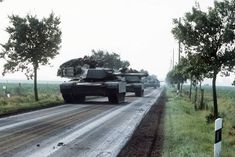 tanks are driving down the road in front of some trees and grass on either side