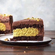 a piece of chocolate cake with yellow and brown frosting on a plate next to another slice