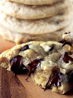 chocolate chip cookies stacked on top of each other next to a wooden cutting board with one broken in half